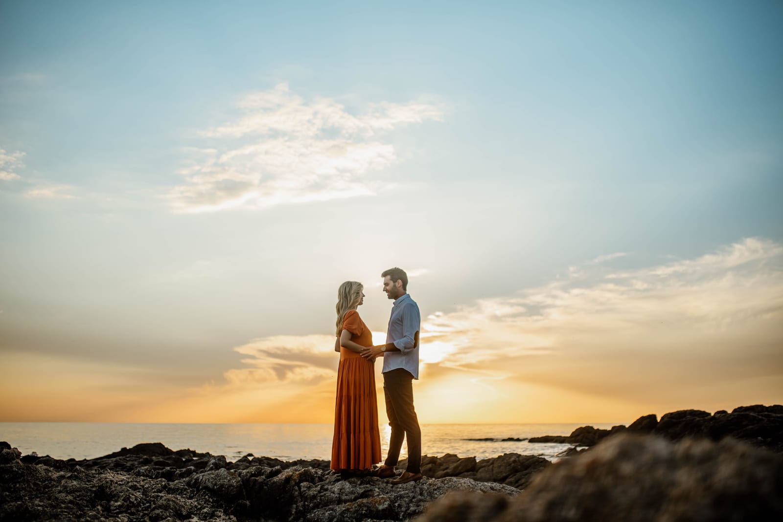 Pablo and pregnant wife on seaside rocks at golden hour