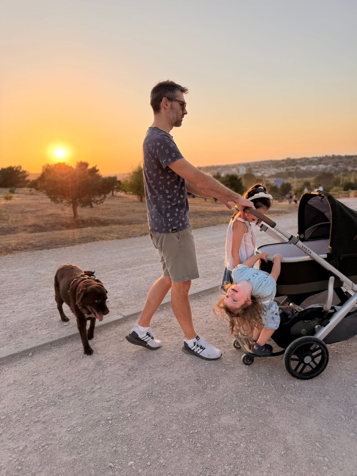 Pablo pushing stroller with daughters and Lola walking at sunset